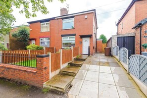 A residential street with houses, a gated driveway, and a narrow sidewalk. - Stylish 3-Bed Home in Leigh | Garden & Parking (Greater Manchester)