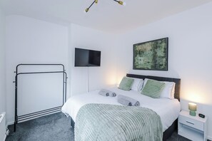 A modern bedroom with a bed, bedside table, TV, and artwork. - Stylish 3-Bed Home in Leigh | Garden & Parking (Greater Manchester)