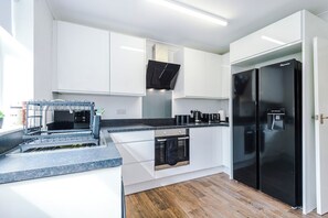 A modern kitchen with white cabinetry, a black refrigerator, and a built-in oven. - Stylish 3-Bed Home in Leigh | Garden & Parking (Greater Manchester)