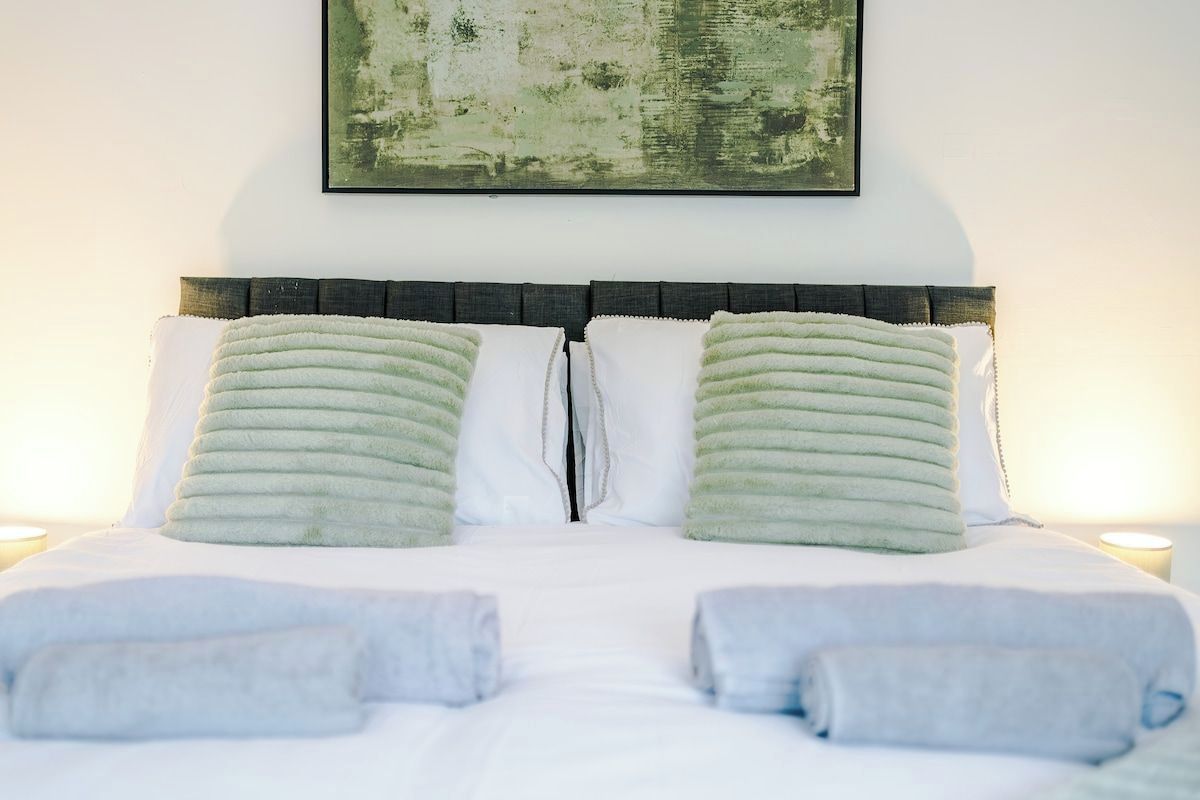 A bed with a headboard, two pillows, and two rolled towels.