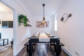 Een eetgedeelte met een lange tafel gedekt voor een maaltijd, een hangende hanglamp en een klok aan de muur.