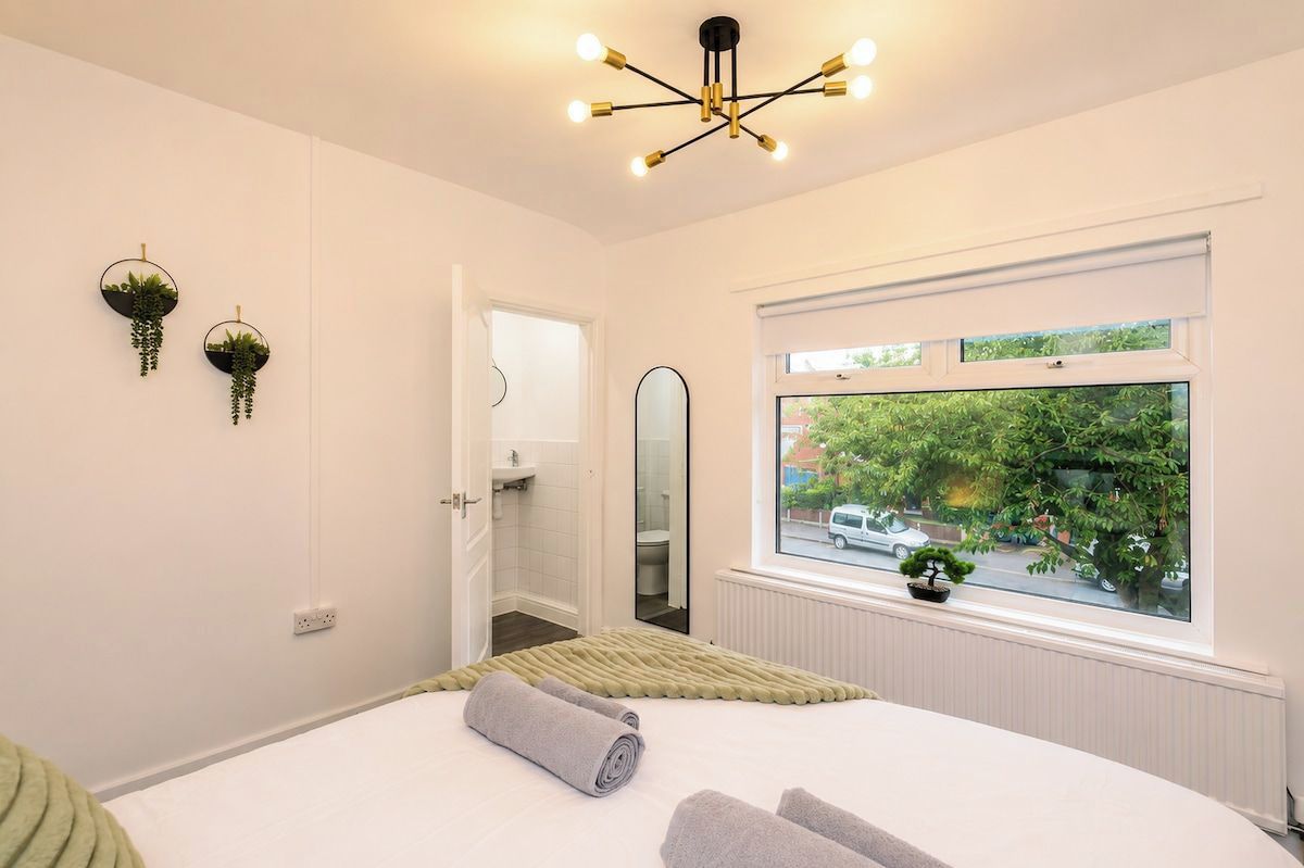 Ein Schlafzimmer mit einem großen Bett, einem Fenster mit Blick auf die Straße und einer modernen Pendelleuchte.