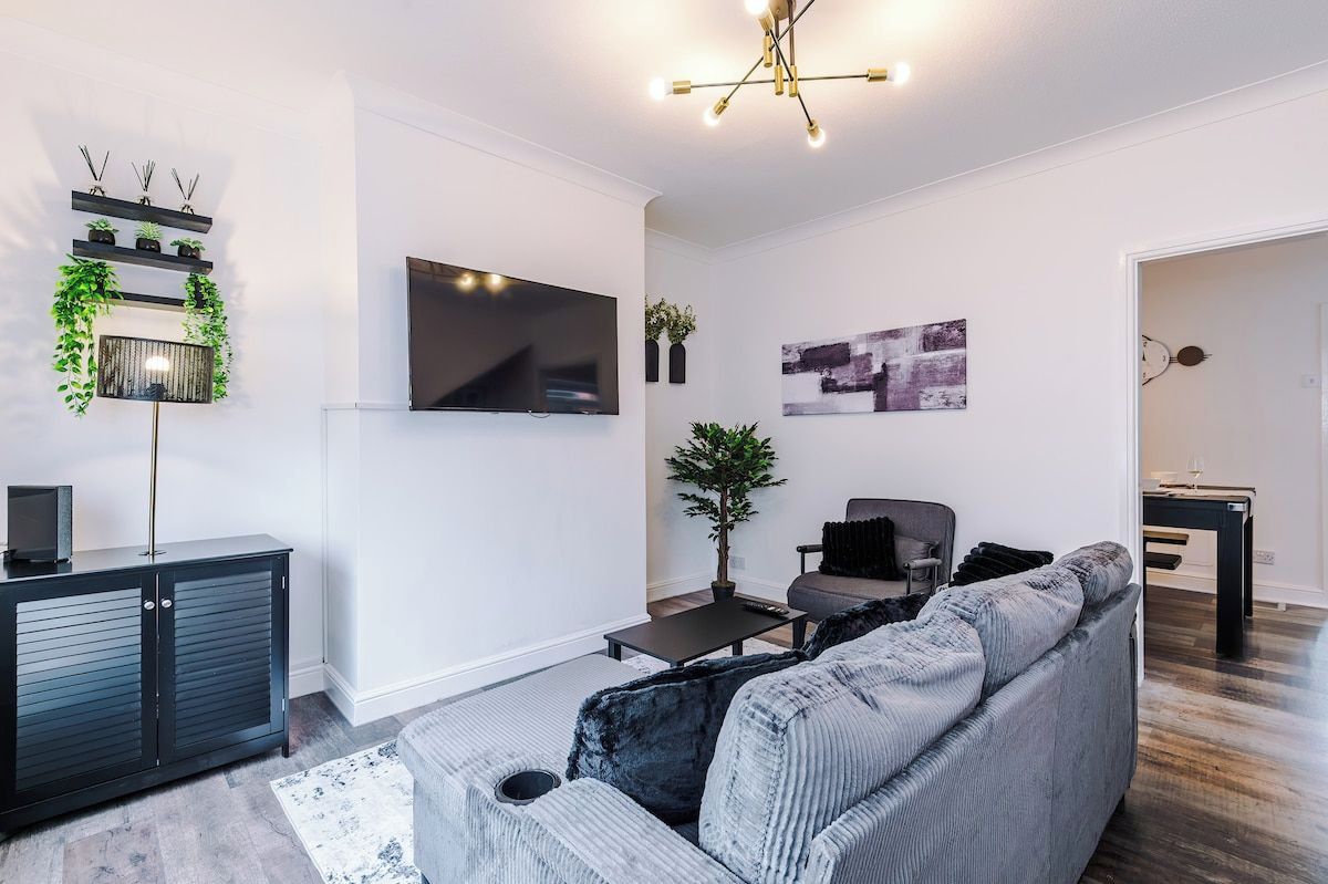 A modern living room with a grey sofa, a flat-screen TV, a coffee table, and a decorative plant.