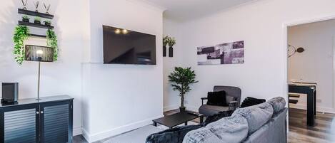 A modern living room with a grey sofa, a flat-screen TV, a coffee table, and a decorative plant.