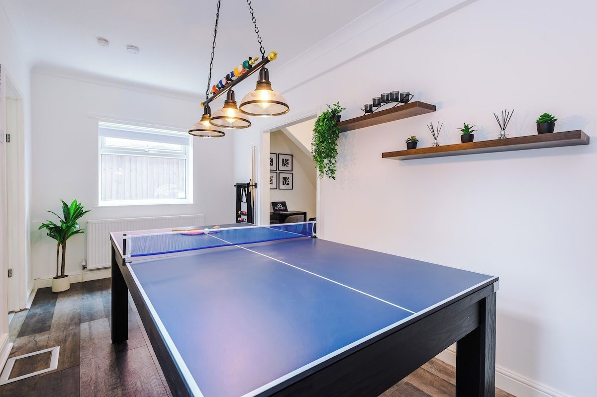 A ping pong table in a room with a window, a hanging plant, and shelves with plants.