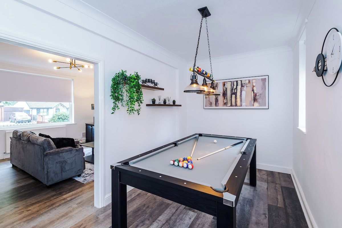 A pool table in a room with a sofa, a hanging plant, and a framed picture on the wall.