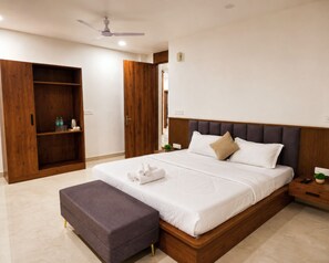 A bedroom with a bed, a wooden wardrobe, a ceiling fan, and a nightstand with a plant. - Shri Radha Bihari by Zenith Suites (Mathura)