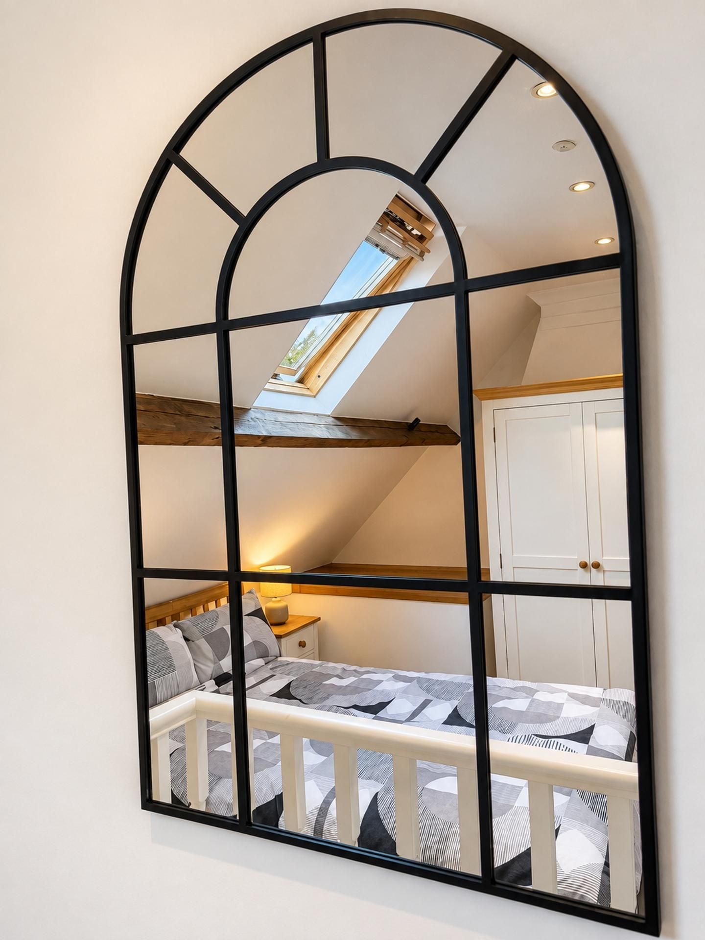 A bedroom with a skylight, a bed with patterned bedding, a nightstand, and a white wardrobe.
