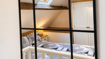 A bedroom with a skylight, a bed with patterned bedding, a nightstand, and a white wardrobe.