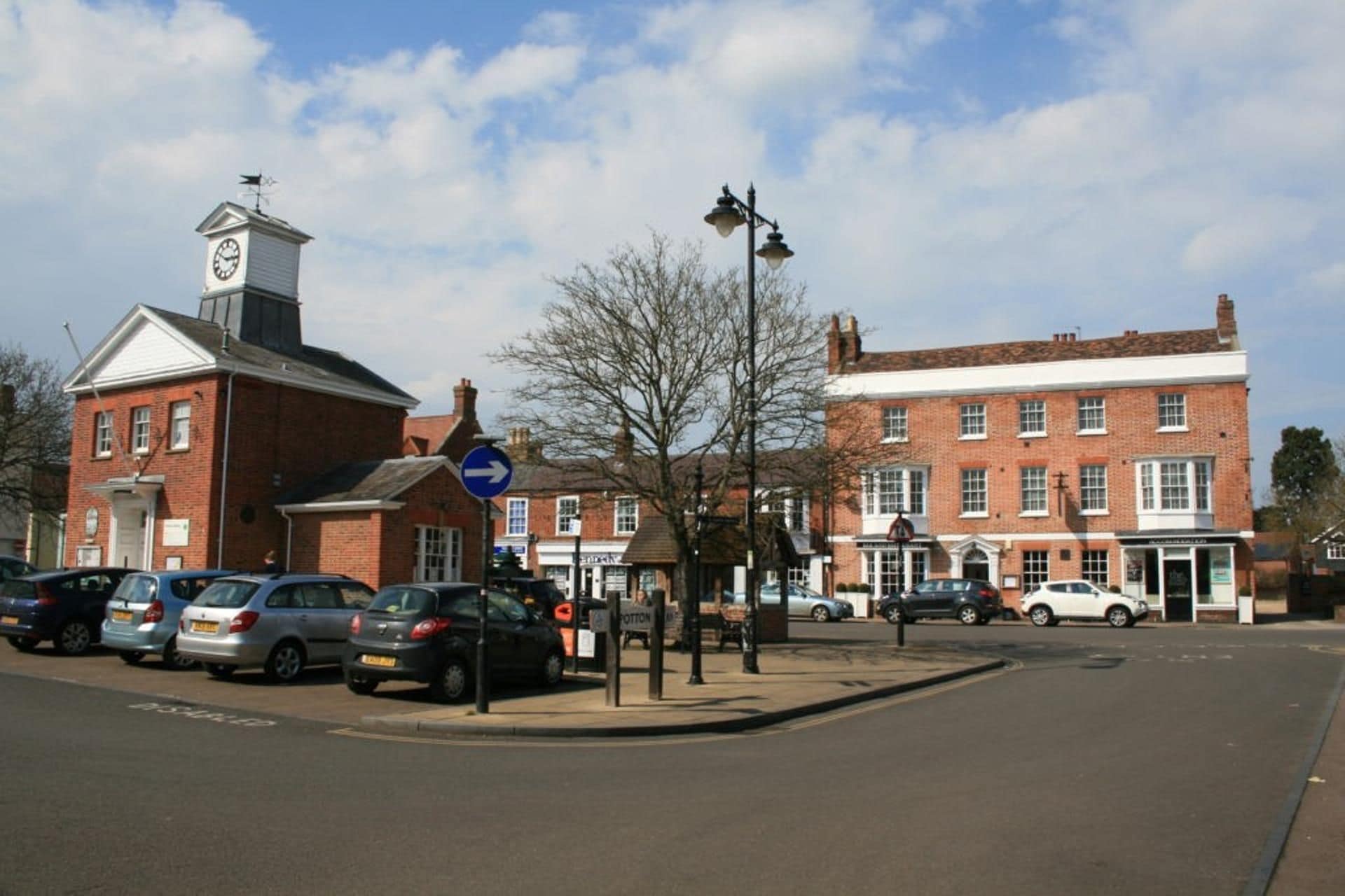 A street with parked cars, a clock tower, and traditional buildings.