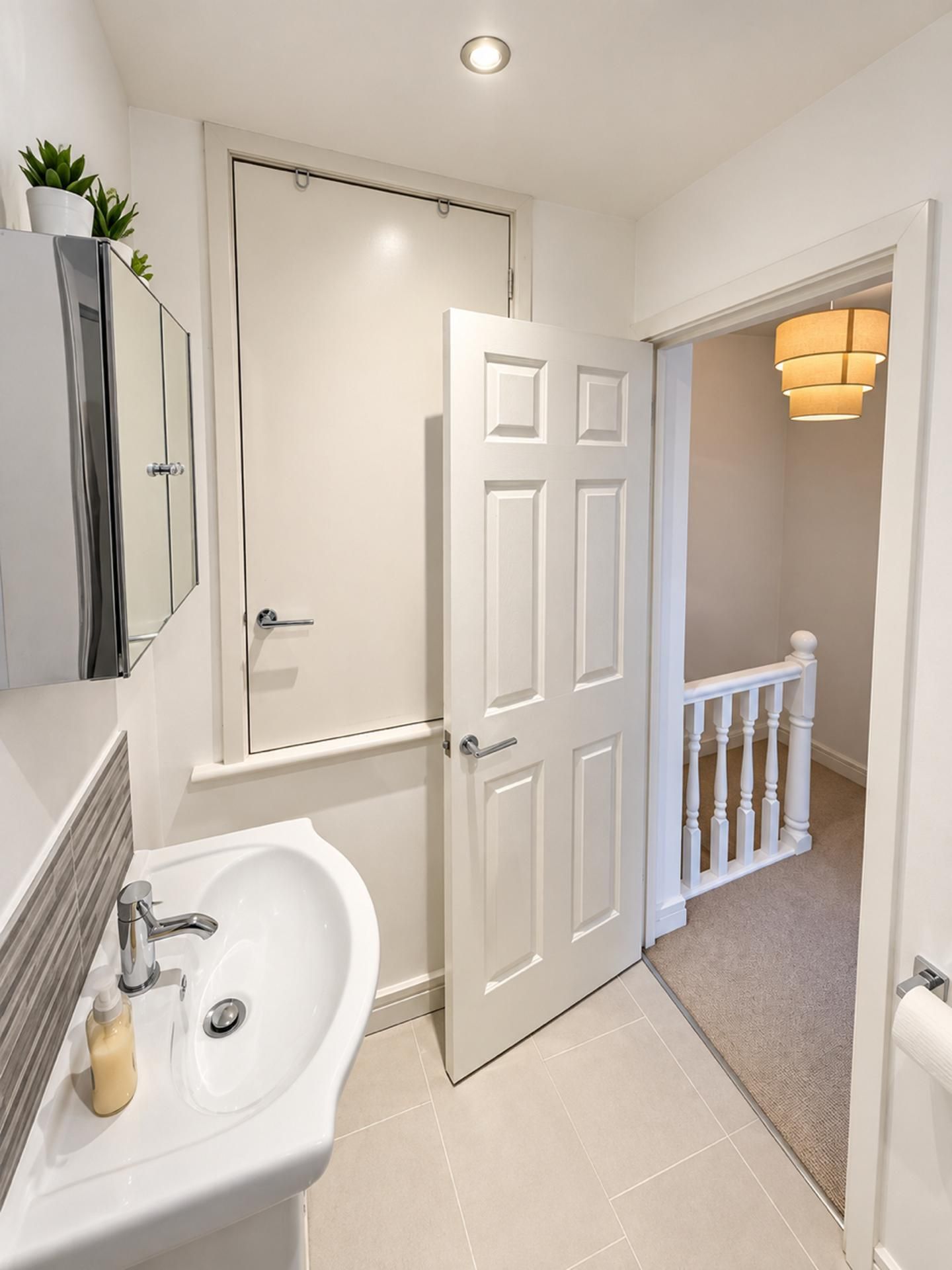 A bathroom with a sink, mirror, and a white door leading to a hallway with a staircase.