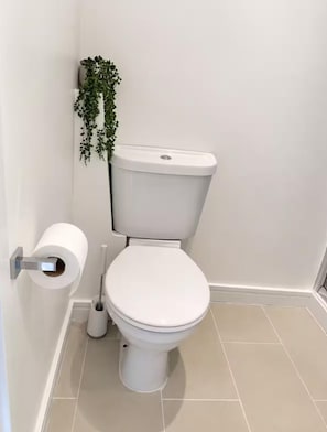 Un inodoro con tapa blanca, un dispensador de papel higiénico y un cepillo de limpieza.