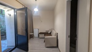 Un pasillo estrecho con una puerta corredera que da a un balcón, un sofá y una pequeña mesa.