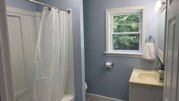 A bathroom with a bathtub, a window, a sink, and a toilet.