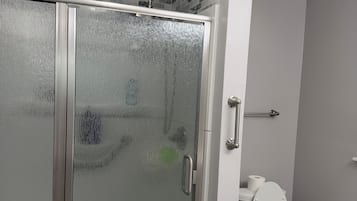 Een badkamer met een douche met glazen wand, een toilet en een prullenbak.