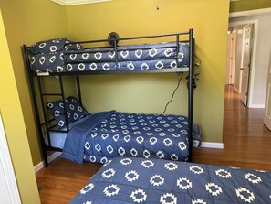 Een stapelbed met een bedspread met patroon en kussens, een ventilator en een houten vloer.