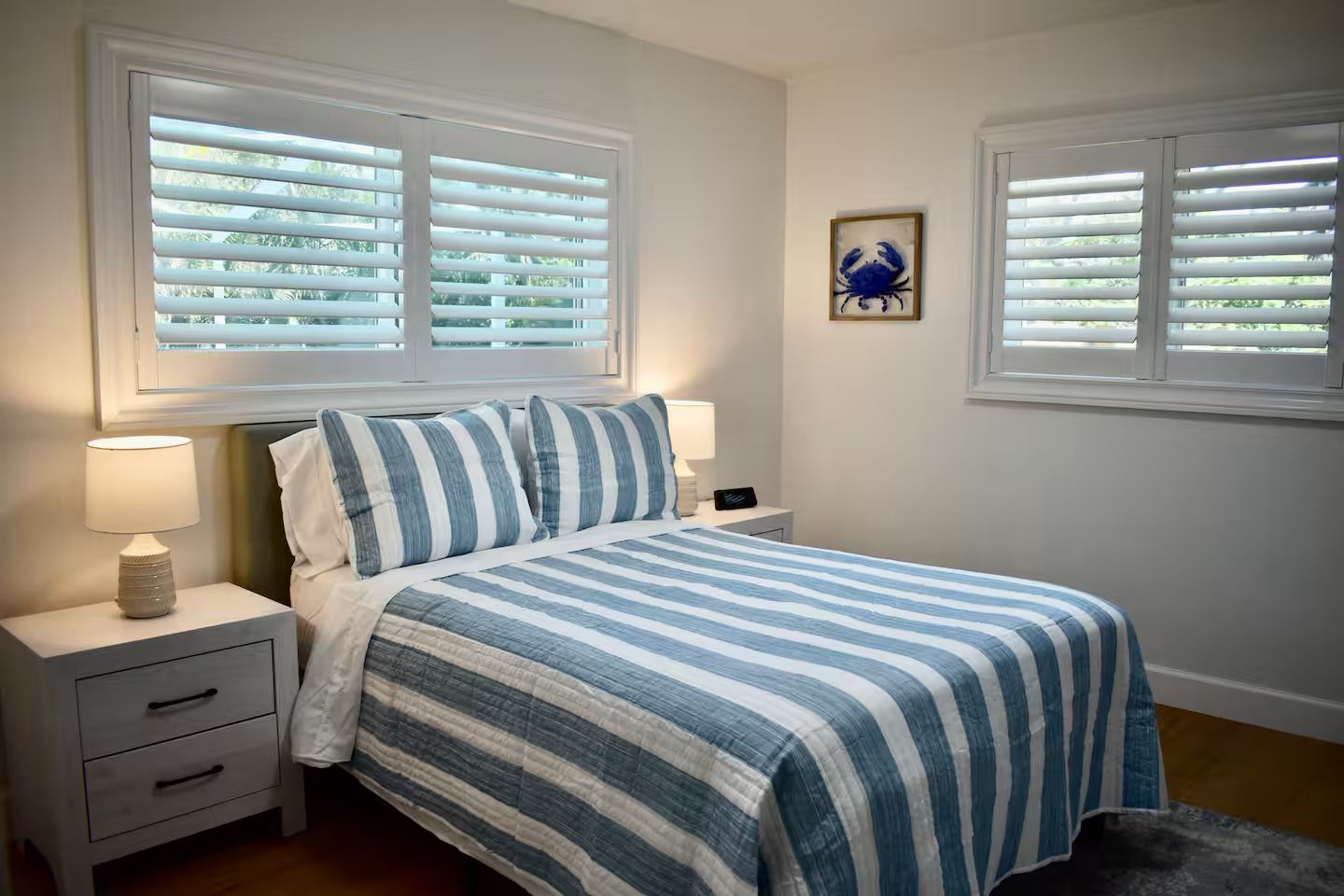 A bedroom with a bed, two bedside tables, a nightstand, a lamp, and a framed picture on the wall.