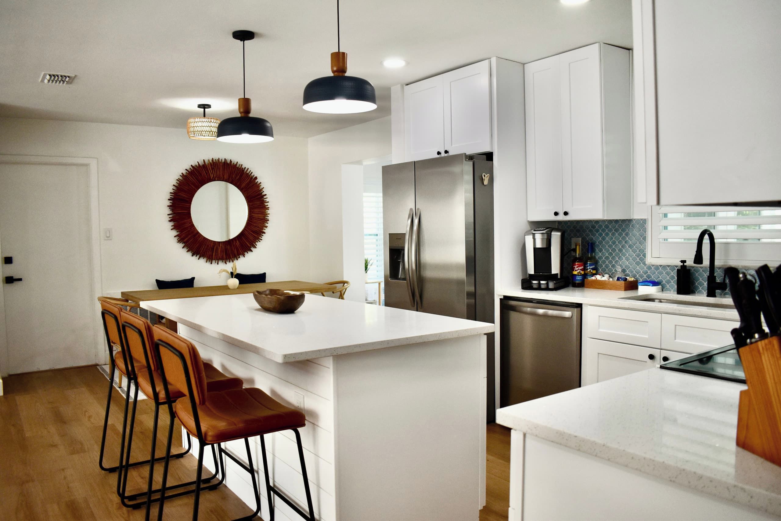 A modern kitchen with white cabinetry, a stainless steel refrigerator, a coffee maker, and a dining area with a wooden table and leather chairs.
