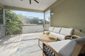 A covered balcony with a sofa and a table, a railing, and a view of trees. - About a 9 min walk to St. Augustine Beach, with easy day trips up the coast (St. Augustine)