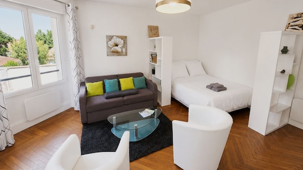 Et moderne, godt oplyst rum med en sofa, en seng, et glasbord og en hvid lænestol.