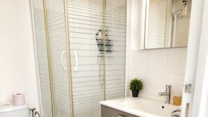 Et moderne badeværelse med en bruseniche med glasvægge, et hvidt toilet og et gråt skab.