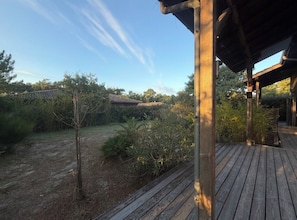 A wooden deck with a view of a garden and a building in the background. - Maison en ossature bois à Vensac Océan (Vensac)