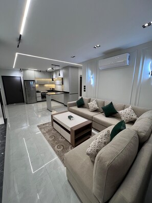 A modern living room with a sofa, coffee table, and a kitchen in the background. - Wonderful 2-bedroom apartment with AC in vibrant Amman (Amman)