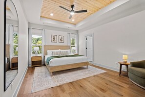 Un dormitorio con cama, mesita de noche, silla, ventilador de techo y ventana con cortinas.
