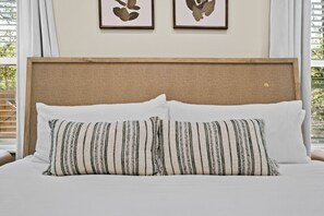 Uma cama com duas almofadas, cabeceira de tecido e obras de arte emolduradas na parede.