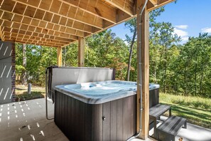 Un jacuzzi bajo una pérgola de madera, con césped y árboles al fondo.
