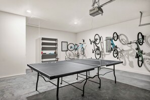 Quarto com mesa de pingue-pongue, bicicletas fixadas na parede e um projetor.