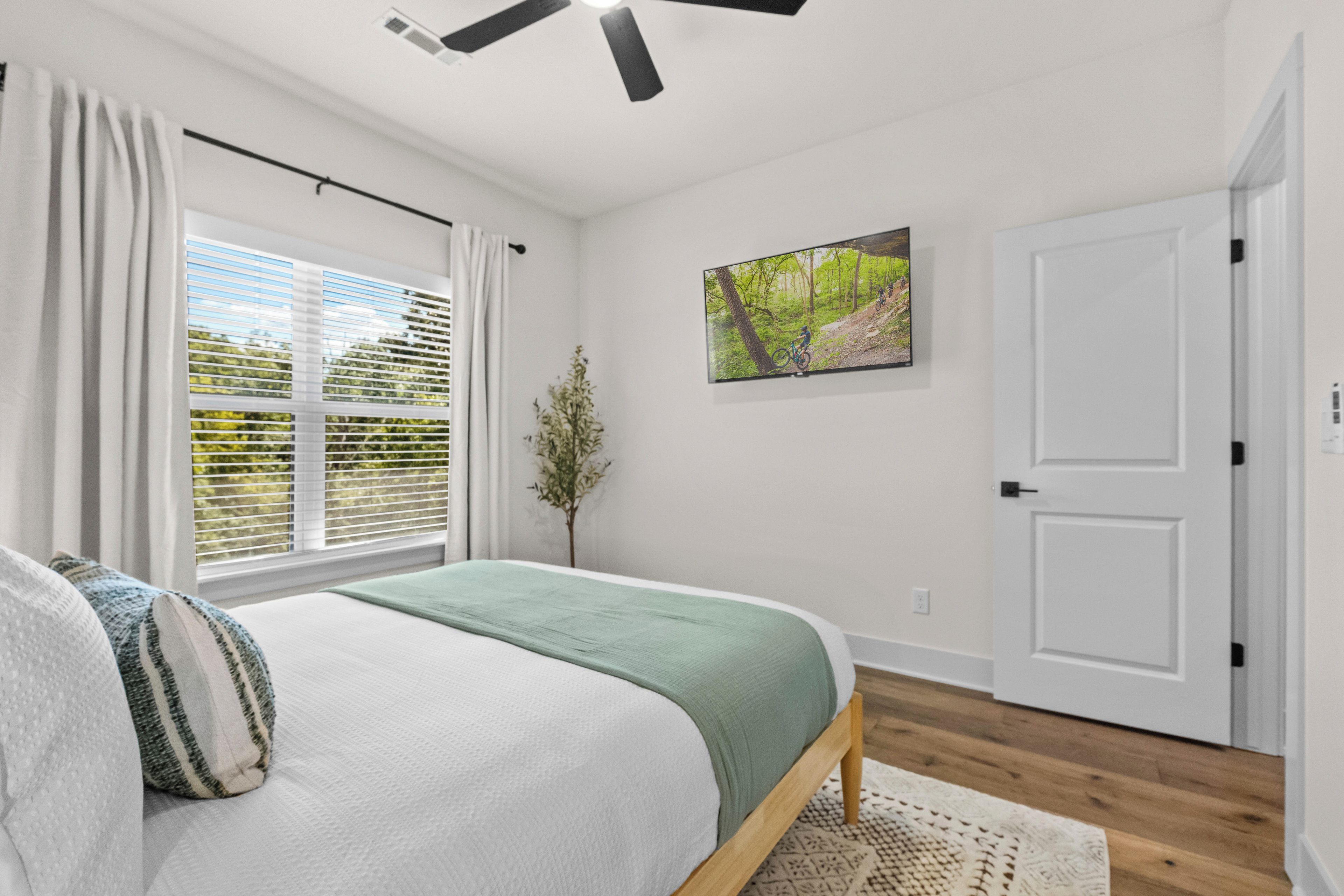 A bedroom with a bed, a window with blinds, a door, and a wall-mounted picture.