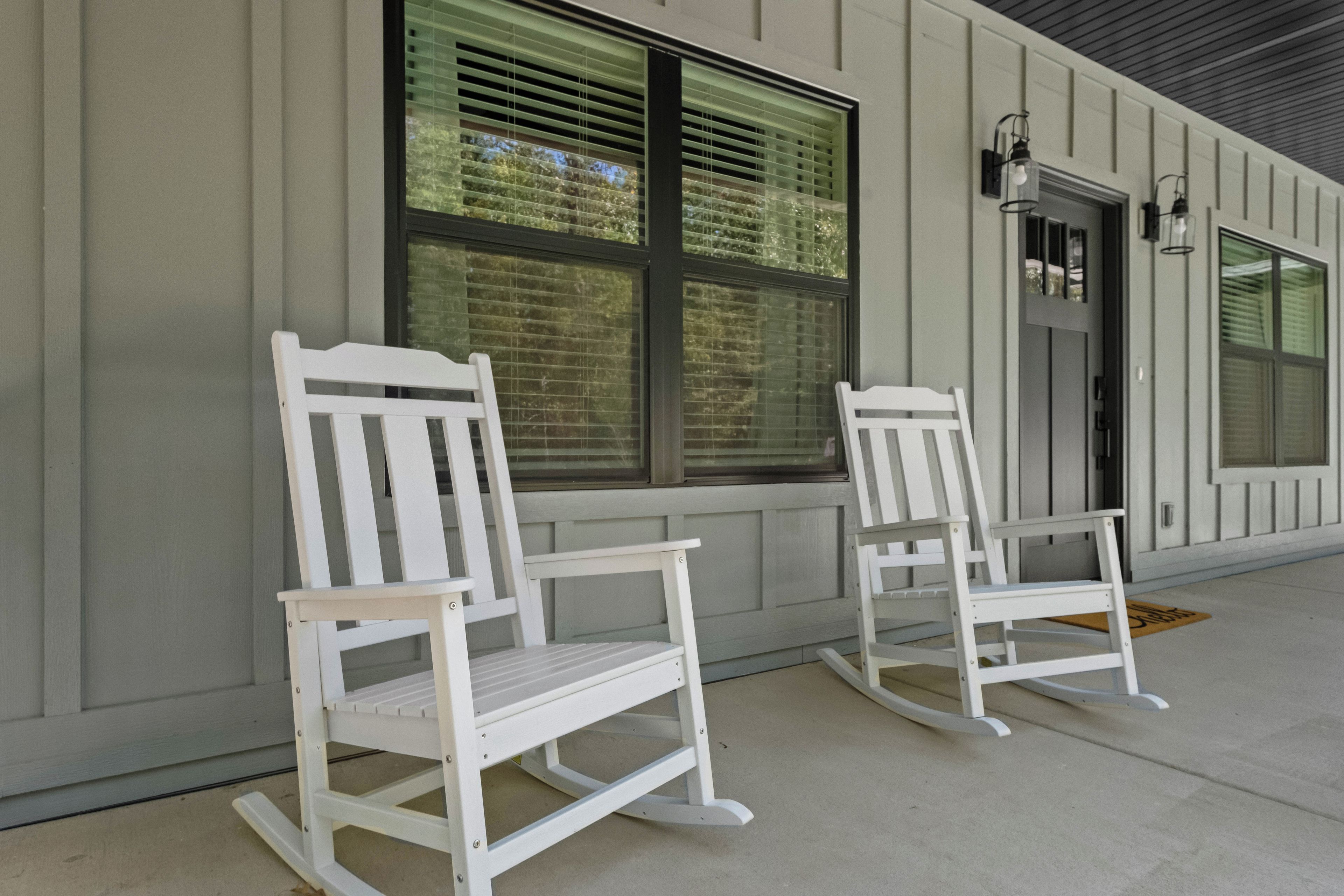 Two white rocking chairs on a porch with a building facade in the background.