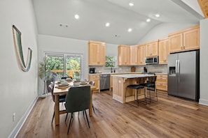 A modern kitchen with wooden cabinets, a stainless steel refrigerator, and a dining area with a table and chairs.