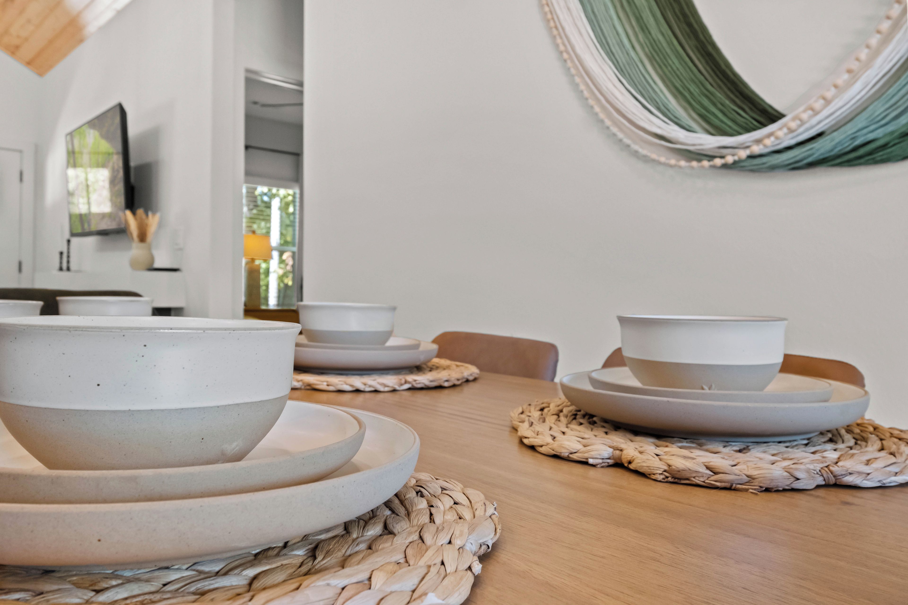 A dining table with ceramic bowls and plates, a woven placemat, and a hammock on the wall.