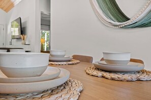 A dining table with ceramic bowls and plates, a woven placemat, and a hammock on the wall.