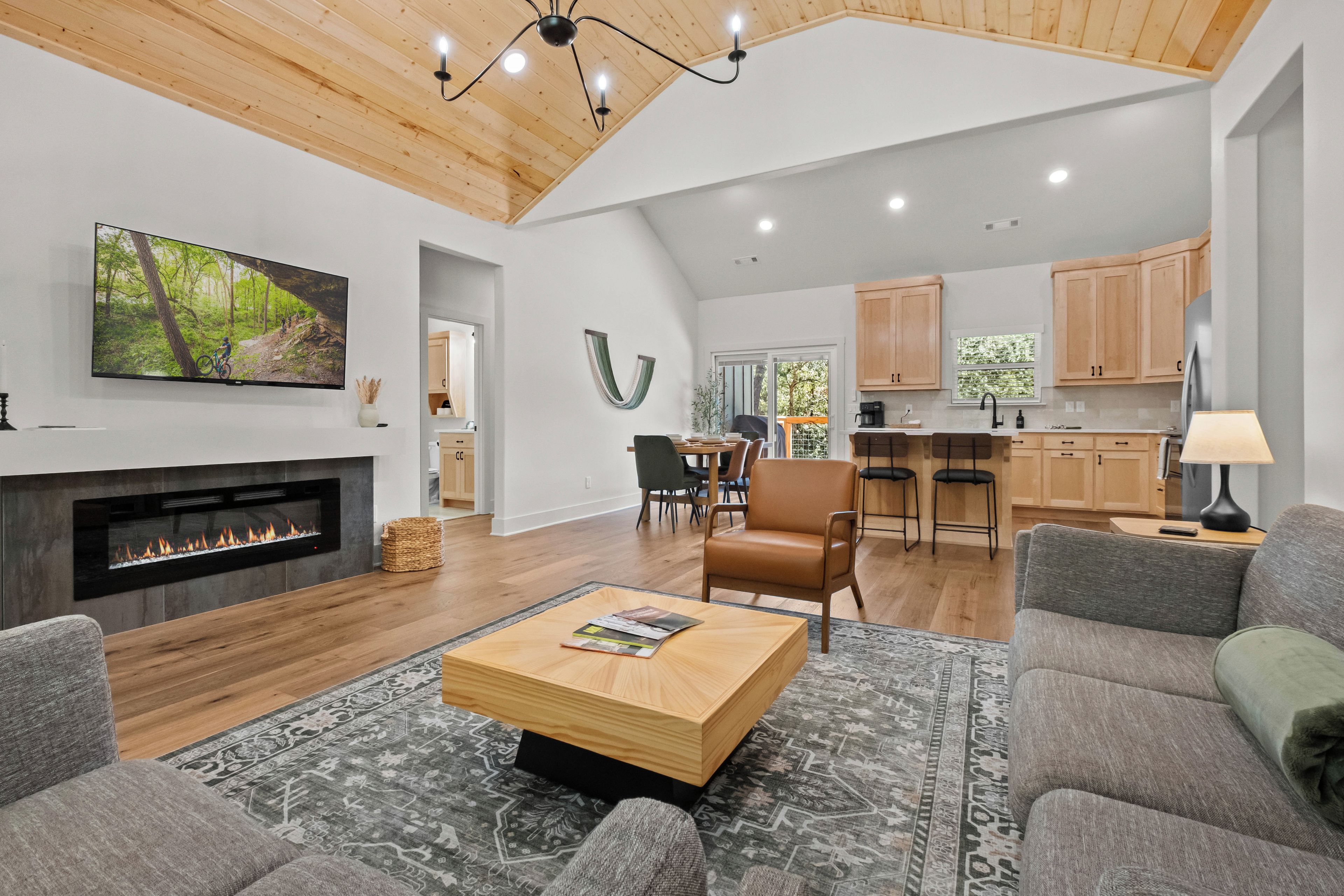 A spacious living area with a fireplace, a television mounted on the wall, and a large window providing natural light.
