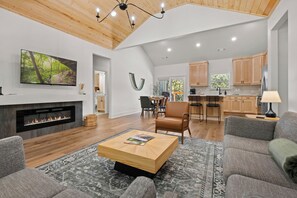 A spacious living area with a fireplace, a television mounted on the wall, and a large window providing natural light.