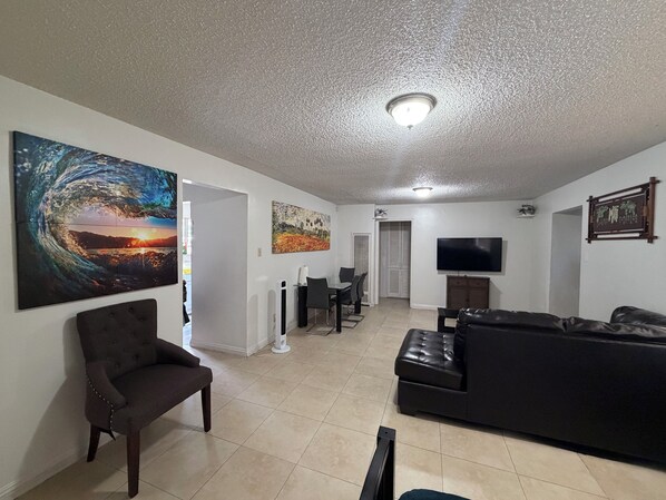 A living room with a black leather sofa, a dark armchair, a flat-screen TV, and artwork on the walls. - Terrific 2-bedroom house with AC in sunny San Gabriel (San Gabriel)