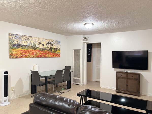 Ein Wohnzimmer mit einem Glastisch, einer schwarzen Ledersofa, einem Flachbildfernseher und einem Bild an der Wand.