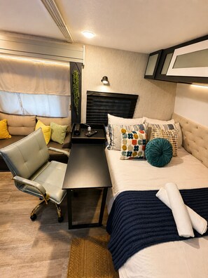 Een kleine slaapkamer met een bed, bureau, stoel en een tafeltje.