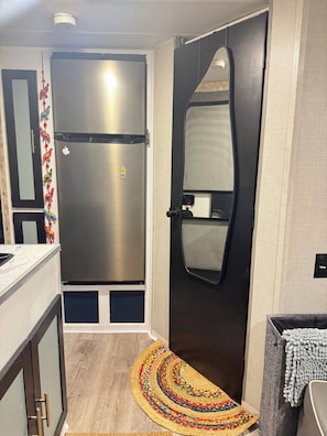 A modern kitchen with a stainless steel refrigerator, a black door, and a colorful woven rug.