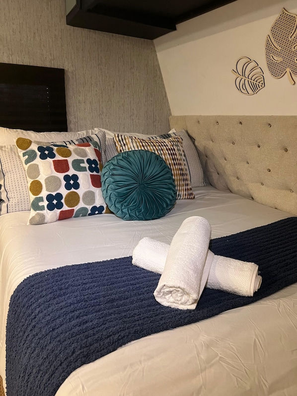 A neatly made bed with a patterned pillow, a teal accent pillow, and a folded towel.