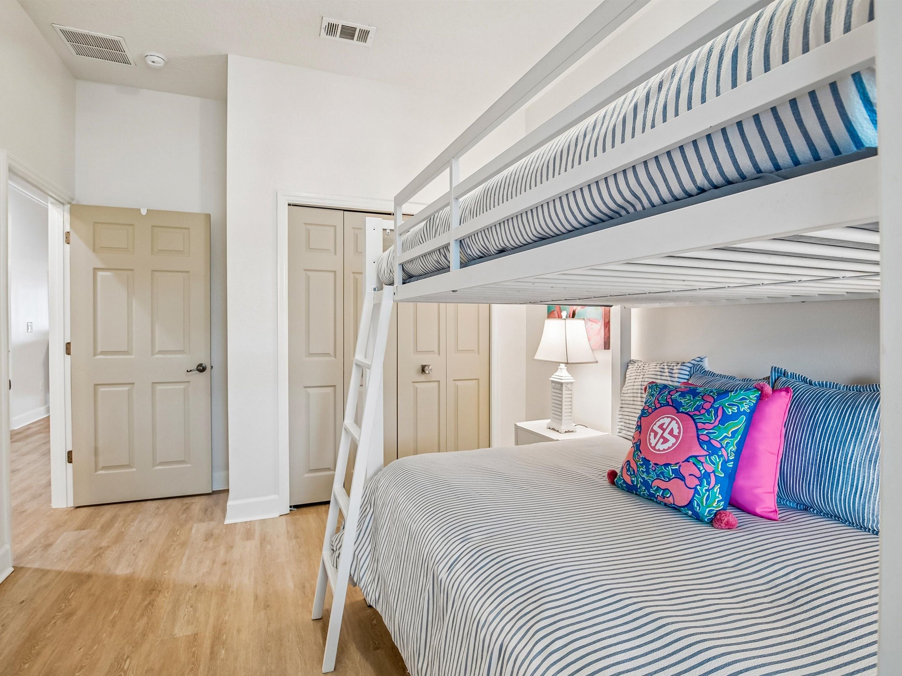 Una cama litera con escalera, una mesita de noche con lámpara y una almohada colorida.