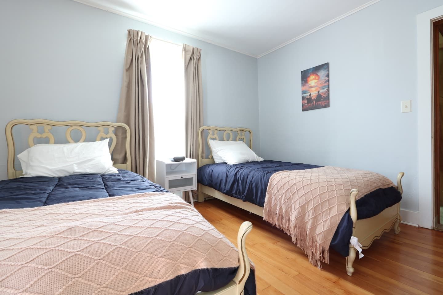 Una habitación con dos camas, una mesita de noche y un cuadro en la pared.
