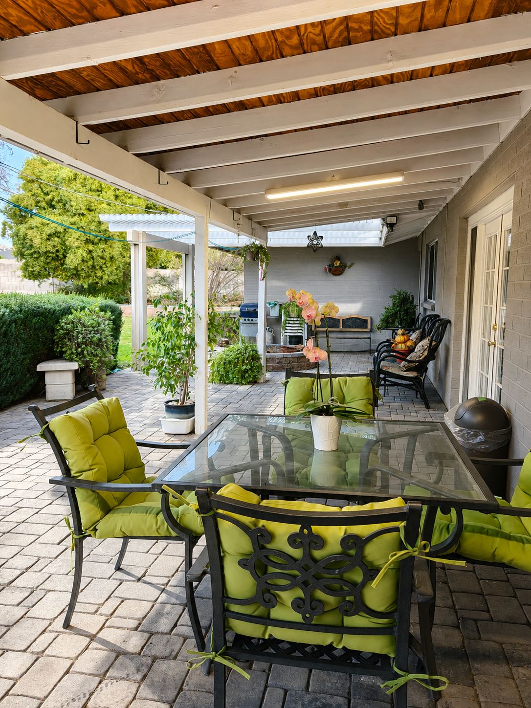 An outdoor patio with a glass table and chairs, a grill, and potted plants.