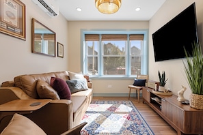 A living room with a brown leather sofa, a patterned rug, a television, and a window with a view of houses. - A peaceful Chicago retreat offering the perfect balance of neighborhood (Chicago)
