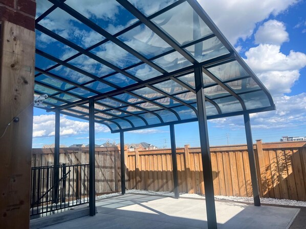A covered outdoor patio with a glass roof, wooden fence, and a clear sky. - Stylish & Newly Built 2 Bedroom Apartment in Milton (Milton)