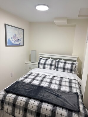 Een slaapkamer met een bed, nachtkastje, speaker en een lijst aan de muur.