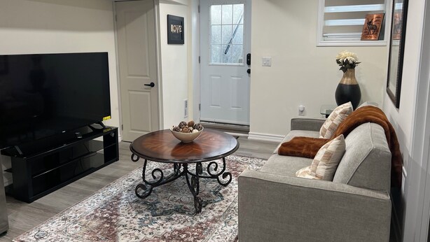 A living room with a flat-screen TV, a coffee table with decorative items, a sofa with cushions, and a patterned rug. - Stylish & Newly Built 2 Bedroom Apartment in Milton (Milton)